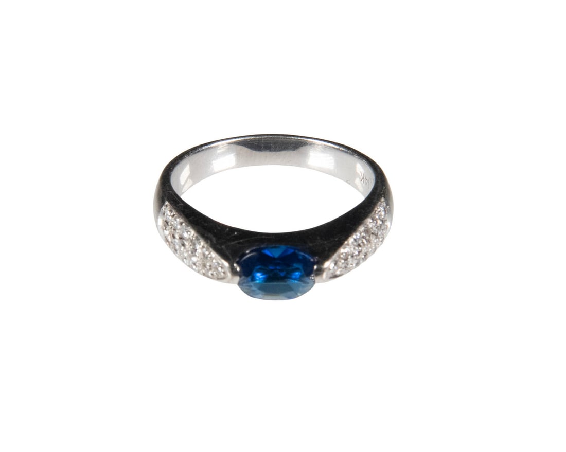 14K WHITE GOLD AND CUBIC ZIRCONIA RING: 14K WHITE GOLD AND CUBIC ZIRCONIA RINGA 14K white gold ring set with an oval faceted blue cubic zirconia, flanked by pav?-set cubic zirconia accents along the shoulders. The design features a gently t