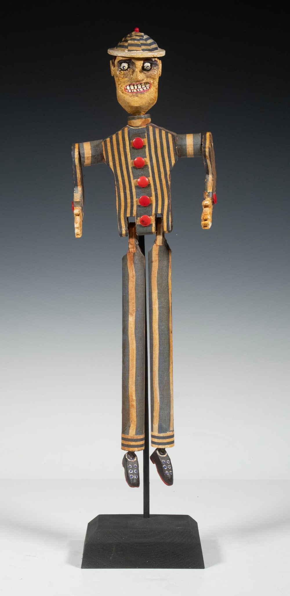HARVEY PETERSON (CONTEMPORARY BELFAST, MAINE): HARVEY PETERSON (CONTEMPORARY BELFAST, MAINE) "Dancing Man in Striped Suit and Hat", carved and painted wood with joints, on black spike stand fitted to loop on back of torso. Height: 22 in. (55.9