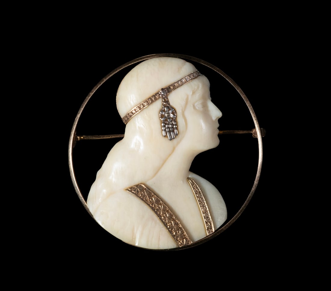 ART DECO 14K GOLD AND CARVED IVORY PROFILE BROOCH: Y ART DECO 14K GOLD AND CARVED IVORY PROFILE BROOCH A finely carved ivory profile depicting a classical female figure in side view, set within a circular 14K gold frame. The figure is adorned with a d