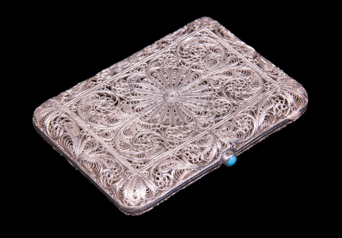 FINE SILVER FILIGREE CASE WITH TURQUOISE CABOCHON: FINE SILVER FILIGREE CASE WITH TURQUOISE CABOCHON A finely worked silver filigree case with intricate scrolling and floral motifs, set with a turquoise cabochon push button. The openwork construction