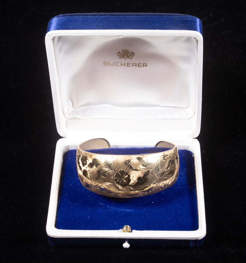 BUCHERER 18K GOLD FLORAL-ENGRAVED CUFF BRACELET: BUCHERER 18K GOLD FLORAL-ENGRAVED CUFF BRACELET An 18K yellow gold cuff bracelet finely engraved with scrolling floral and foliate motifs, the surface exhibiting a soft satin finish that enhances the
