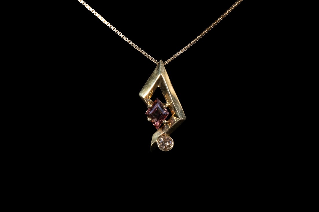 CUSTOM DESIGN 18K GOLD, TOURMALINE, AND COLOR DIAMOND NECKLACE: CUSTOM DESIGN 18K GOLD, TOURMALINE, AND COLOR DIAMOND NECKLACE A modernist pendant featuring a lozenge-cut pink tourmaline and a round brilliant-cut yellowish-brown diamond, mounted in a geometric 18K
