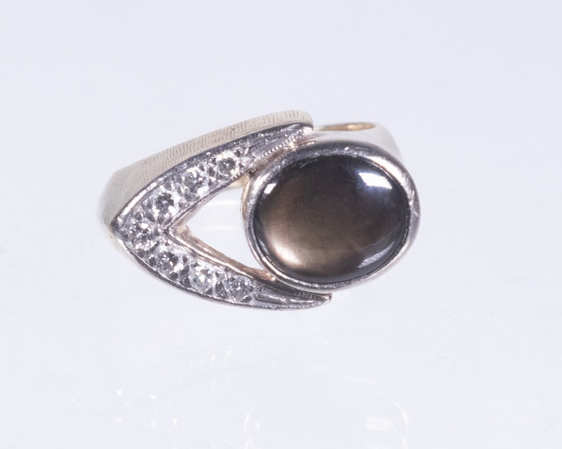 14K GOLD CAT S-EYE GEMSTONE AND DIAMOND RING: 14K GOLD CAT S-EYE GEMSTONE AND DIAMOND RING A 14K yellow gold ring set with an oval cabochon cat s-eye gemstone displaying a distinct chatoyant band, framed by a sculptural white gold accent