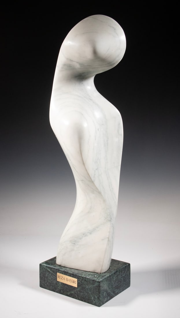 REZA BASSIRI (IRAN/CANADA, 20TH CENTURY): REZA BASSIRI (IRAN/CANADA, 20TH CENTURY) Hooded Woman, in grey streaked white marble on green marble base, signed lower back. Nametag on base. Size: 33 1/2 x 8 x 9 in. (85.1 x 20.3 x 22.9 cm.)