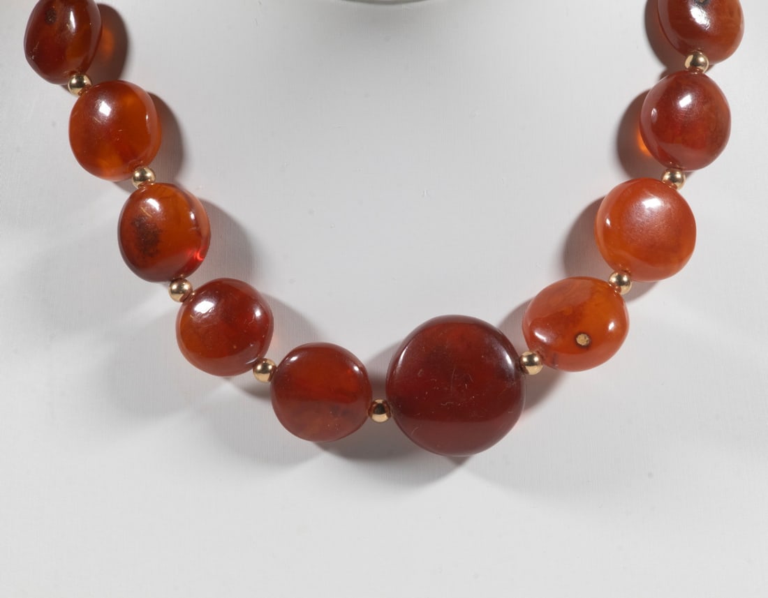 VINTAGE AMBER BEAD NECKLACE: VINTAGE AMBER BEAD NECKLACE A vintage necklace composed of (25) graduated round and flattened amber beads in warm cognac and honey tones, separated by small gold-tone spacer beads. The amber beads mea