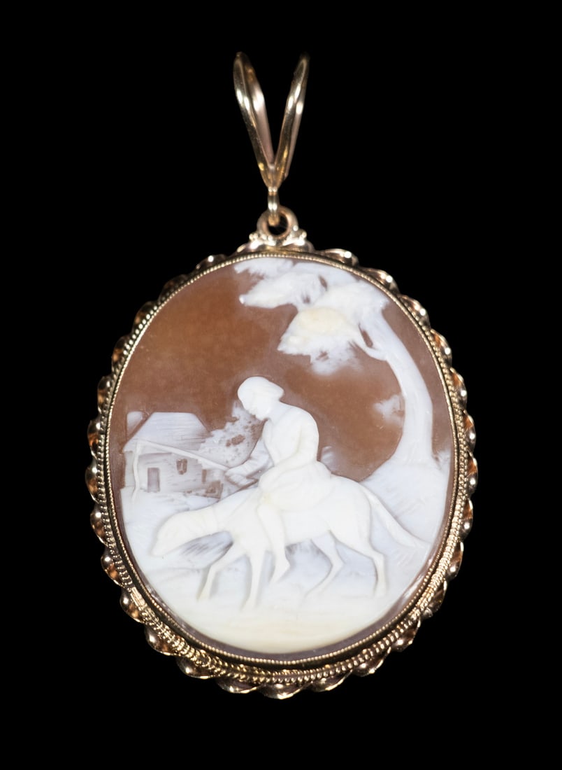 14K GOLD SHELL CAMEO PENDANT: 14K GOLD SHELL CAMEO PENDANT A 14K gold pendant set with a large oval carved shell cameo, depicting a rider on horseback in a landscape with a house and tree. The cameo carved in white relief against 