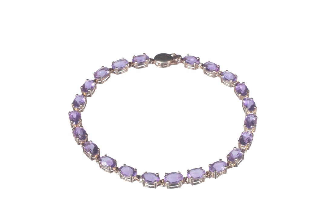 10K GOLD AMETHYST TENNIS BRACELET: 10K GOLD AMETHYST TENNIS BRACELET A 10K gold tennis bracelet set with (22) oval-cut amethysts, each measuring approximately 6.22 x 4.21 mm. The stones display a pleasing medium lavender to violet hue 