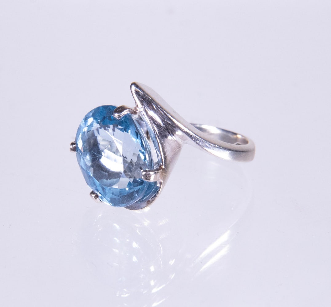 14K GOLD LARGE BLUE TOPAZ RING: 14K GOLD LARGE BLUE TOPAZ RING A 14K white gold ring set with a large oval-cut blue topaz measuring approximately 14.92 x 12.69 mm, displaying a bright and vibrant sky-blue hue. The interior of the sh