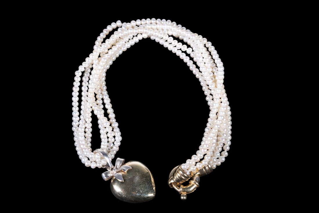 THREE-STRAND SEED PEARL NECKLACE WITH SILVER HEART PENDANT: THREE-STRAND SEED PEARL NECKLACE WITH SILVER HEART PENDANT A three-strand necklace composed of small seed pearls, joined by a sterling silver clasp. Suspending a heart-form pendant with bow surmount w