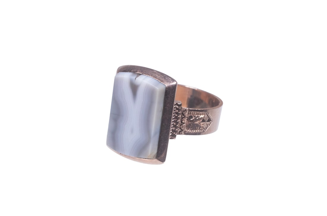 VICTORIAN 14K ROSE GOLD AND BANDED AGATE RING: VICTORIAN 14K ROSE GOLD AND BANDED AGATE RING A 14K rose gold ring set with a modified rectangular banded agate plaque displaying natural gray and white striations. The shoulders decorated with engrav