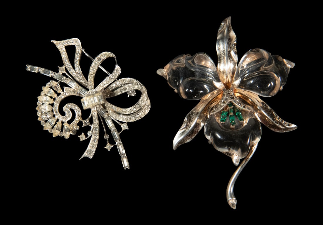 (2) AMERICAN VINTAGE COSTUME JEWELRY TRIFARI AND CHARLES REIS BROOCHES: (2) AMERICAN VINTAGE COSTUME JEWELRY TRIFARI AND CHARLES REIS BROOCHES Comprising a Trifari gold-tone floral brooch with molded clear Lucite petals, accented by clear and emerald-colored rhinestones, 