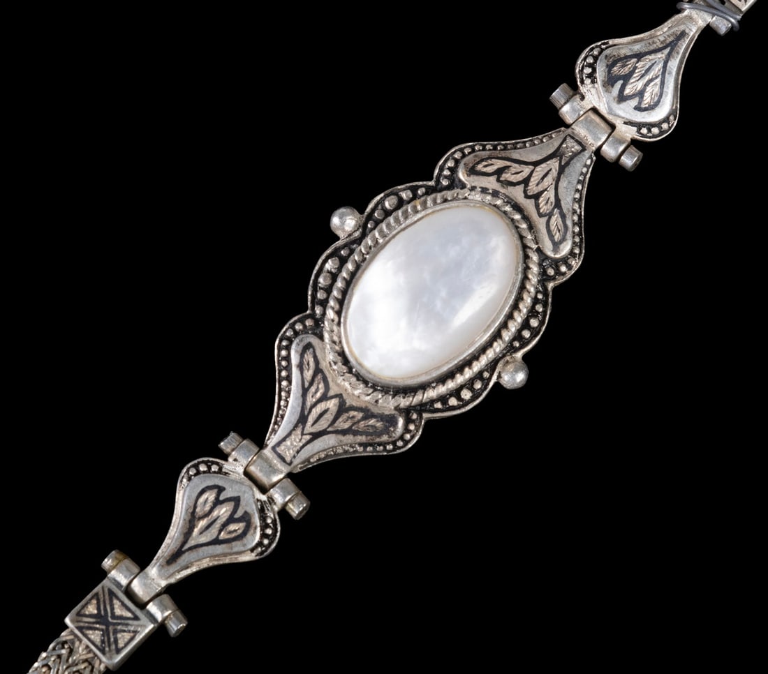 STERLING SILVER, MOTHER-OF-PEARL AND NIELLO INLAY BRACELET: STERLING SILVER, MOTHER-OF-PEARL AND NIELLO INLAY BRACELET A sterling silver bracelet featuring an oval mother-of-pearl cabochon set within an articulated link design. The surrounding panels are