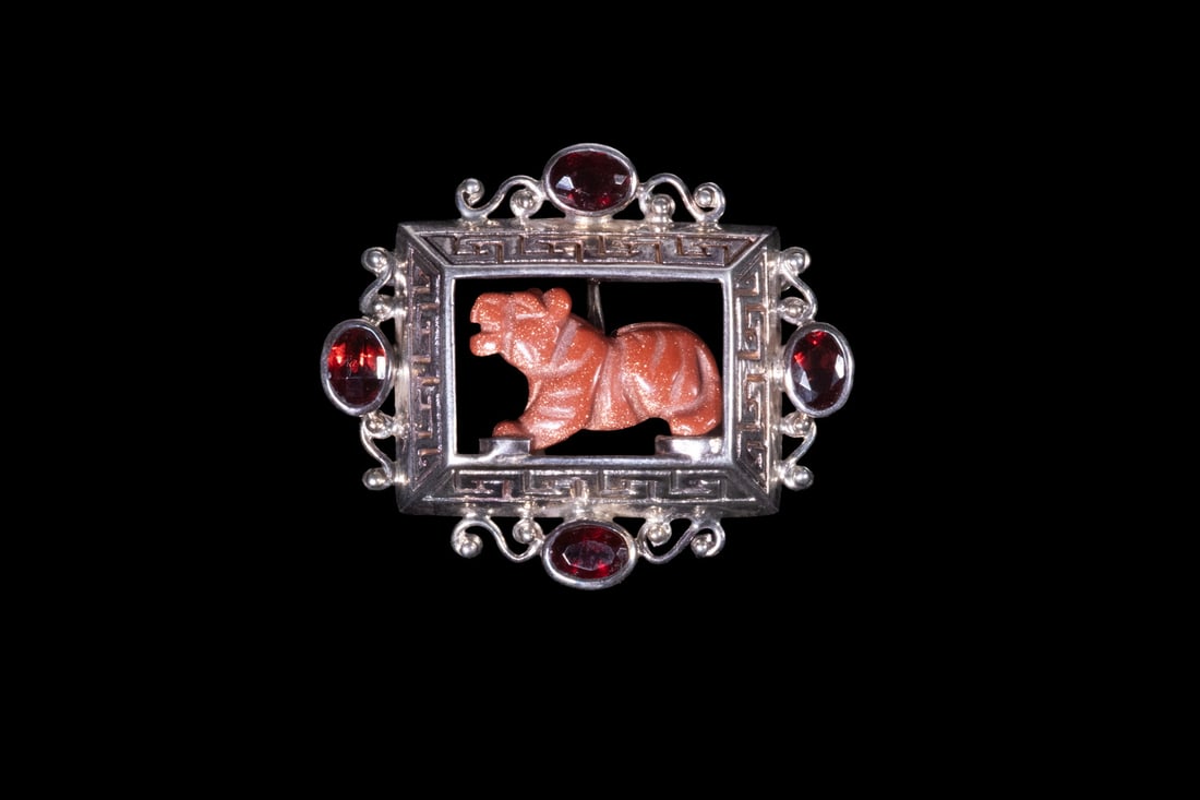 STERLING SILVER, GARNET, AND GOLDSTONE TIGER PENDANT/BROOCH: STERLING SILVER, GARNET, AND GOLDSTONE TIGER PENDANT/BROOCH A sterling silver convertible pendant/brooch featuring an openwork rectangular frame set with (4) faceted red garnets. The center suspends