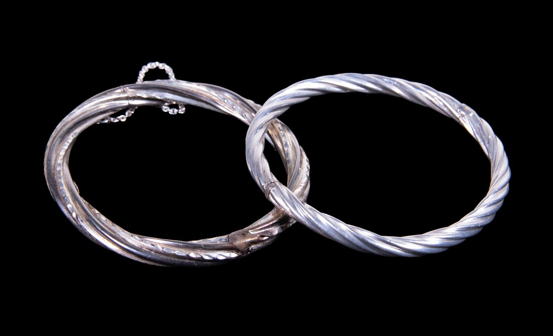 (2) STERLING SILVER HINGED BANGLE BRACELETS: (2) STERLING SILVER HINGED BANGLE BRACELETS A group of two sterling silver hinged bangle bracelets, including one with engraved decoration and safety chain, and one of twisted rope form. Both with