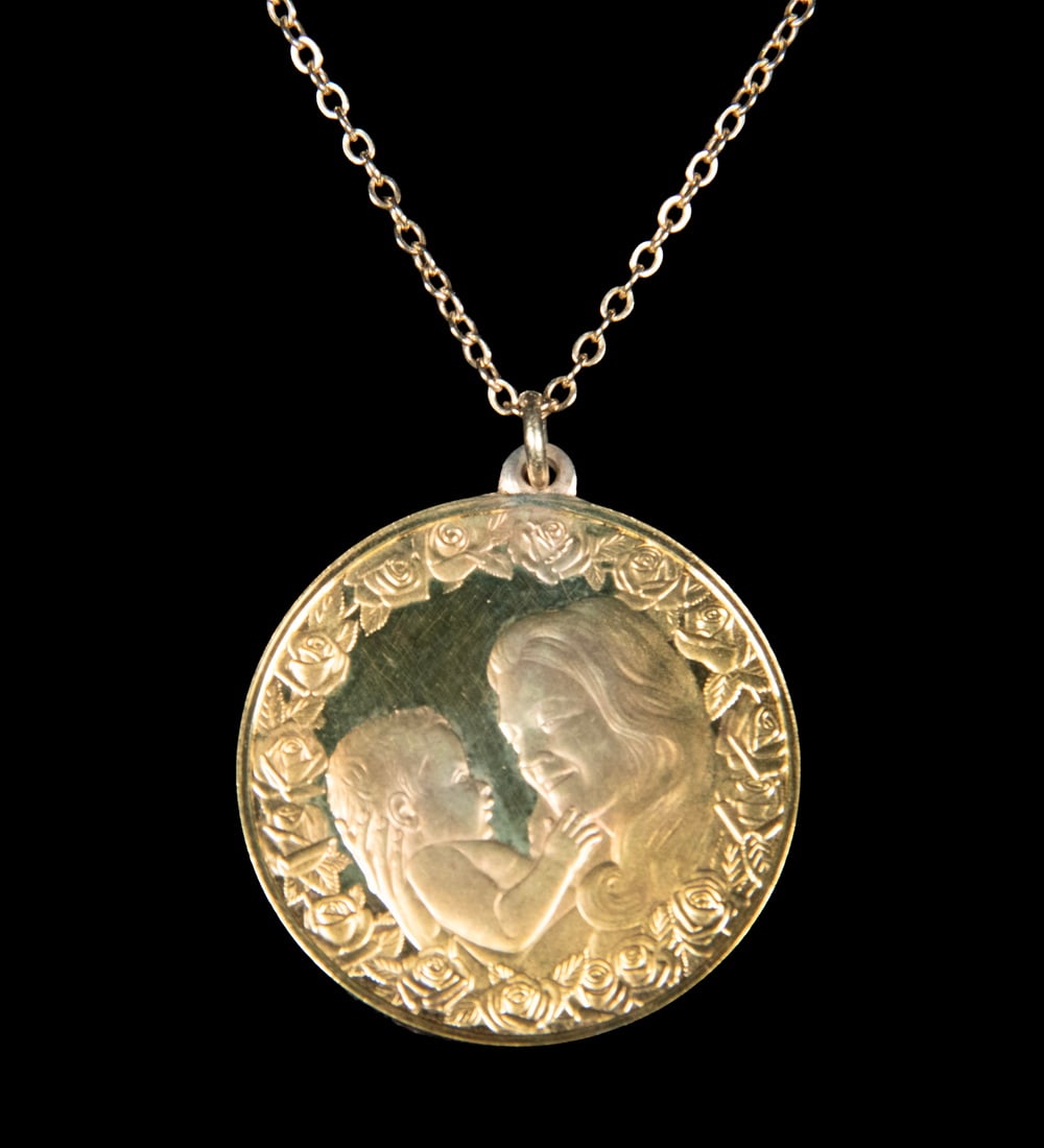 STERLING SILVER MOTHER’S DAY PENDANT NECKLACE: STERLING SILVER MOTHER’S DAY PENDANT NECKLACE A gilded sterling silver pendant necklace featuring a round medallion engraved with a mother and child within a border of roses. The reverse inscribed