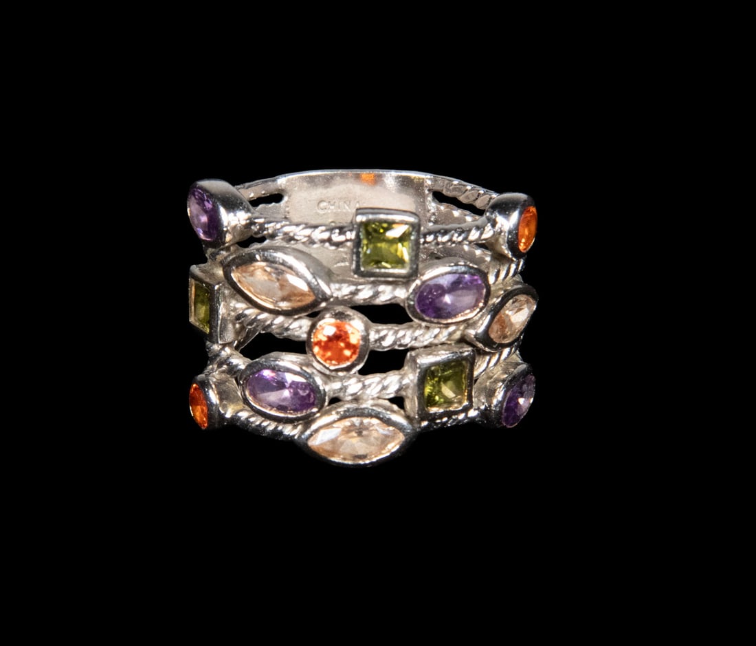 STERLING SILVER MULTI-GEMSTONE RING: STERLING SILVER MULTI-GEMSTONE RING A wide sterling silver ring set with an array of faceted gemstones including citrine, amethyst, and peridot, arranged in alternating shapes and bezels with rope-edg