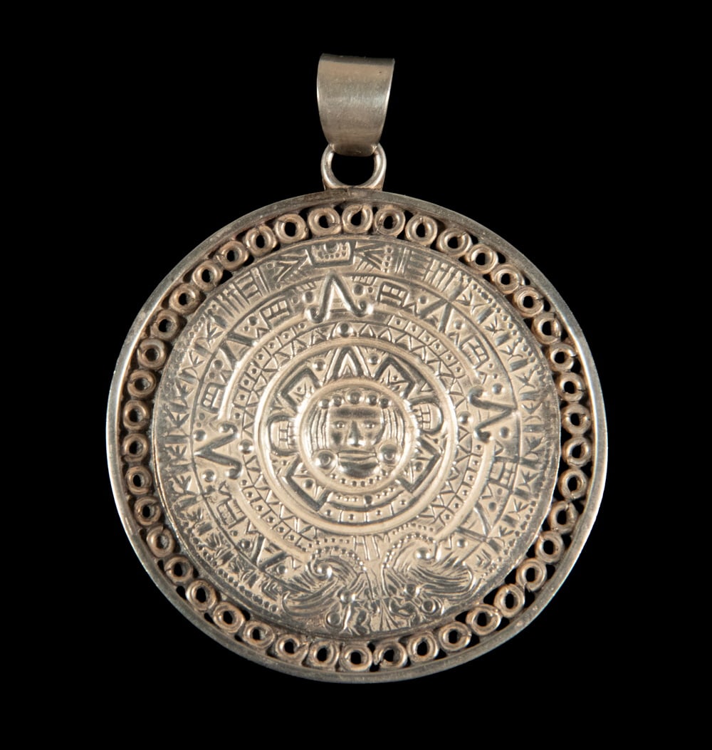 MEXICAN STERLING SILVER AZTEC CALENDAR PENDANT: MEXICAN STERLING SILVER AZTEC CALENDAR PENDANT Circular sterling silver pendant decorated with an Aztec calendar motif in relief, centered by a stylized sun deity mask and surrounded by geometric and 