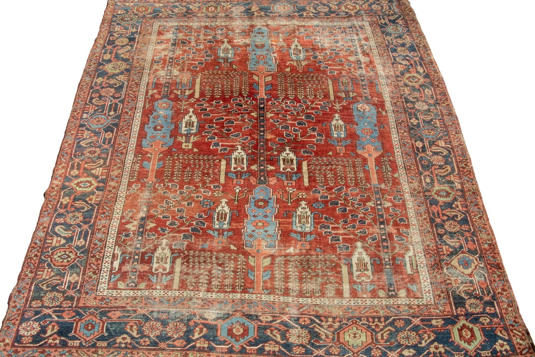HERIZ RUG (10'8" x 9'4"): HERIZ RUG (10'8" x 9'4") An offering of a vintage Heriz rug. Features a central tree design on the red field accompanied by palmettes and vine motifs with a blue palmette border. Large areas of wear.