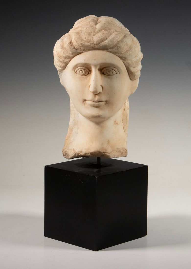ROMAN STYLE MARBLE BUST OF WOMAN: ROMAN STYLE MARBLE BUST OF WOMAN Grand Tour Era, hand carved Bust of Aristocratic Woman with ornate coiffure, with fractured lower edge. On black cube museum mount. OS: 15 1/2 x 6 1/2 x 5 1/2 in. (39.