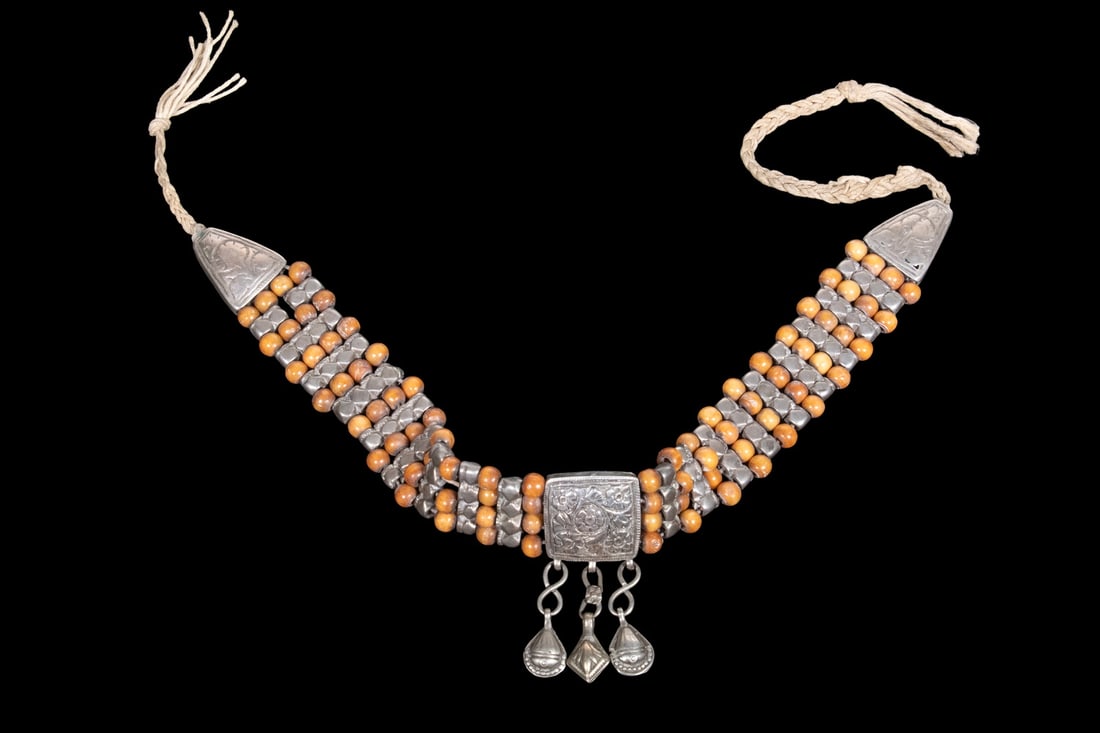 MOROCCAN SILVER AND BEAD NECKLACE: MOROCCAN SILVER AND BEAD NECKLACE Composed of multiple strands of silver spacers and natural bead elements, centered by a square repouss? plaque with three pendant bell drops. 4.36 ozt. tw. Overall
