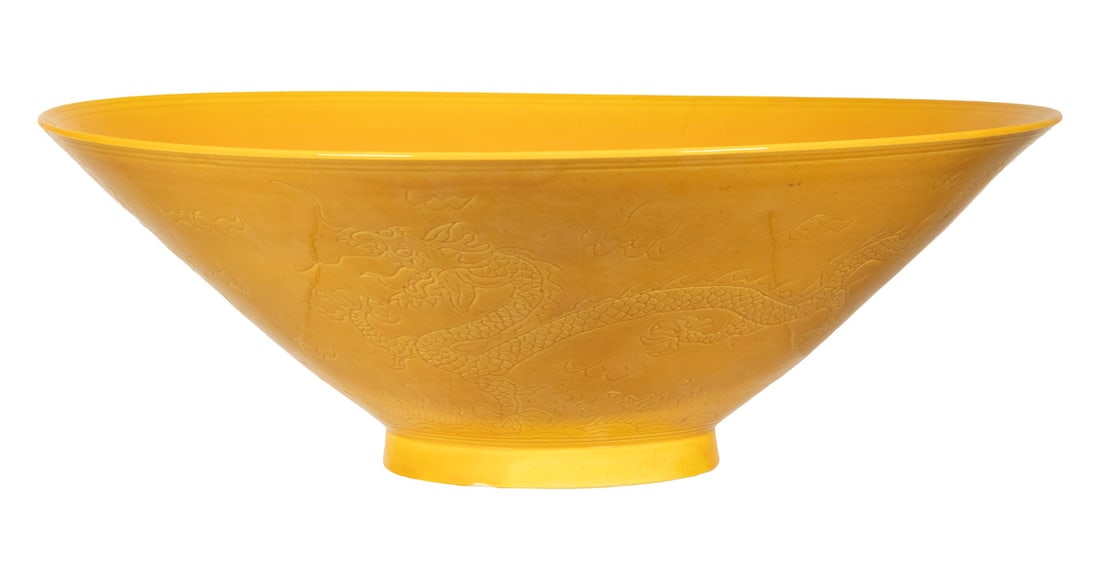 CHINESE YELLOW-GLAZED MOLDED DRAGON BOWL: CHINESE YELLOW-GLAZED MOLDED DRAGON BOWL A Chinese porcelain bowl covered in a bright yellow glaze and molded in low relief with dragons amidst clouds and waves. The underside bearing a six-character
