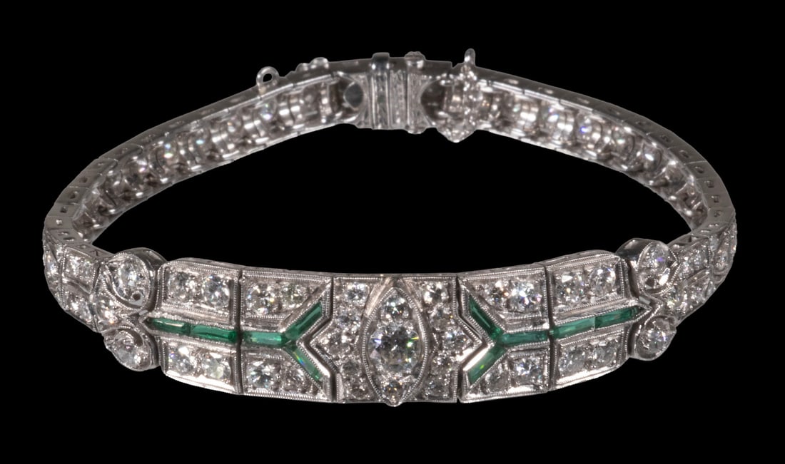 ART DECO PLATINUM, DIAMOND, AND EMERALD BRACELET: ART DECO PLATINUM, DIAMOND, AND EMERALD BRACELET A platinum bracelet of geometric Art Deco design, set with (76) round-cut diamonds, centering one measuring approximately 4.21 mm. Accented by (10)