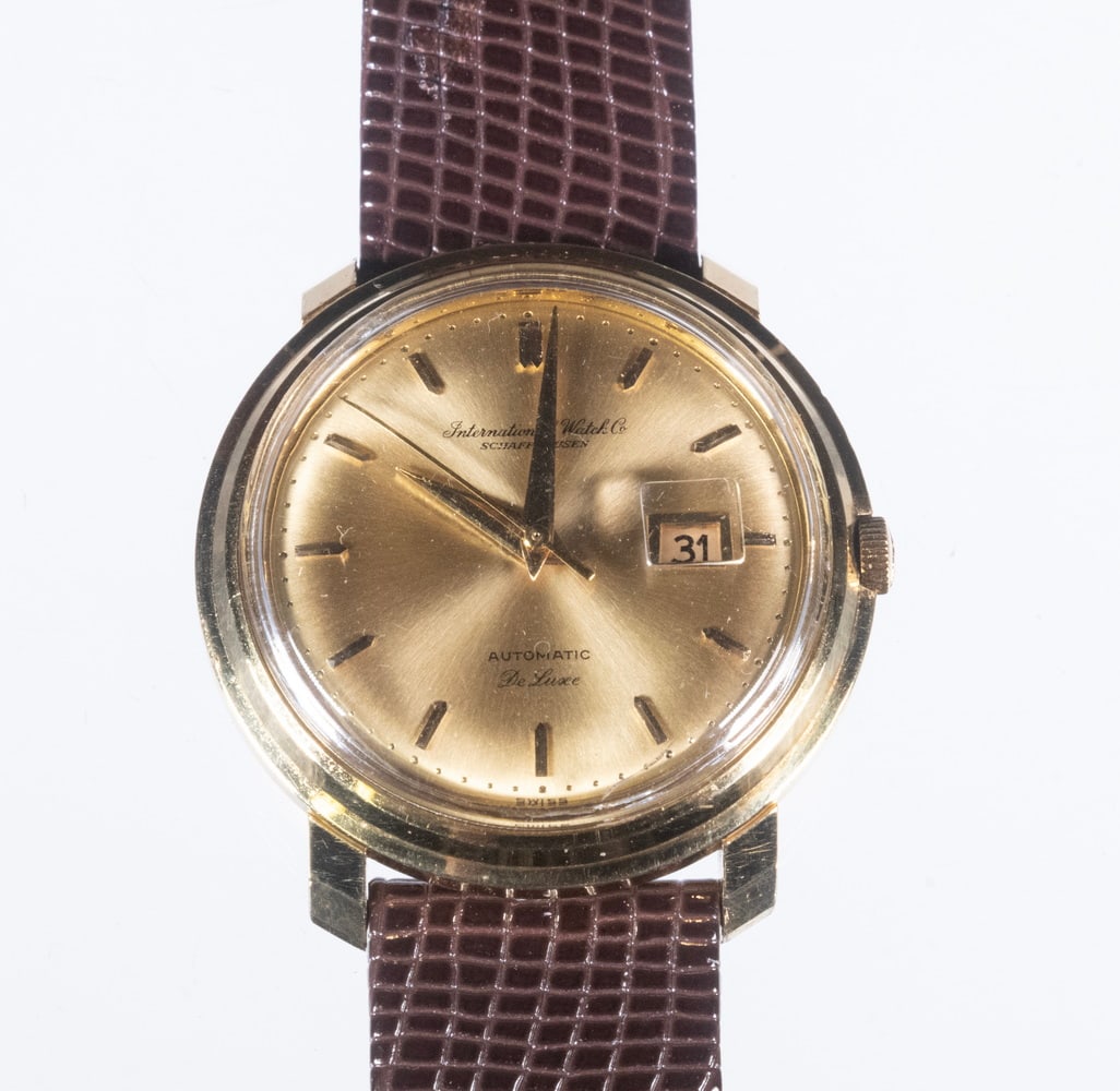 INTERNATIONAL WATCH CO. 18K GOLD AUTOMATIC DE LUXE WRISTWATCH: 18K GOLD AND DIAMOND BROOCH An elegant 18K gold brooch designed as a flowing arrangement of textured ribbon-like loops, accented by a round brilliant-cut diamond measuring approximately 4.12 mm and