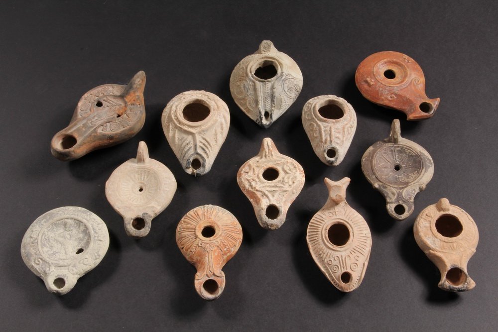 (12) ANCIENT MIDDLE EASTERN LAMPS - Roman & Palestinian: (12) ANCIENT MIDDLE EASTERN LAMPS - Roman & Palestinian Pottery Lamps, all decorated, encrusted, six with finger loops or tabs, one with standing human figure, one with proto-Islamic designs. Roughly 