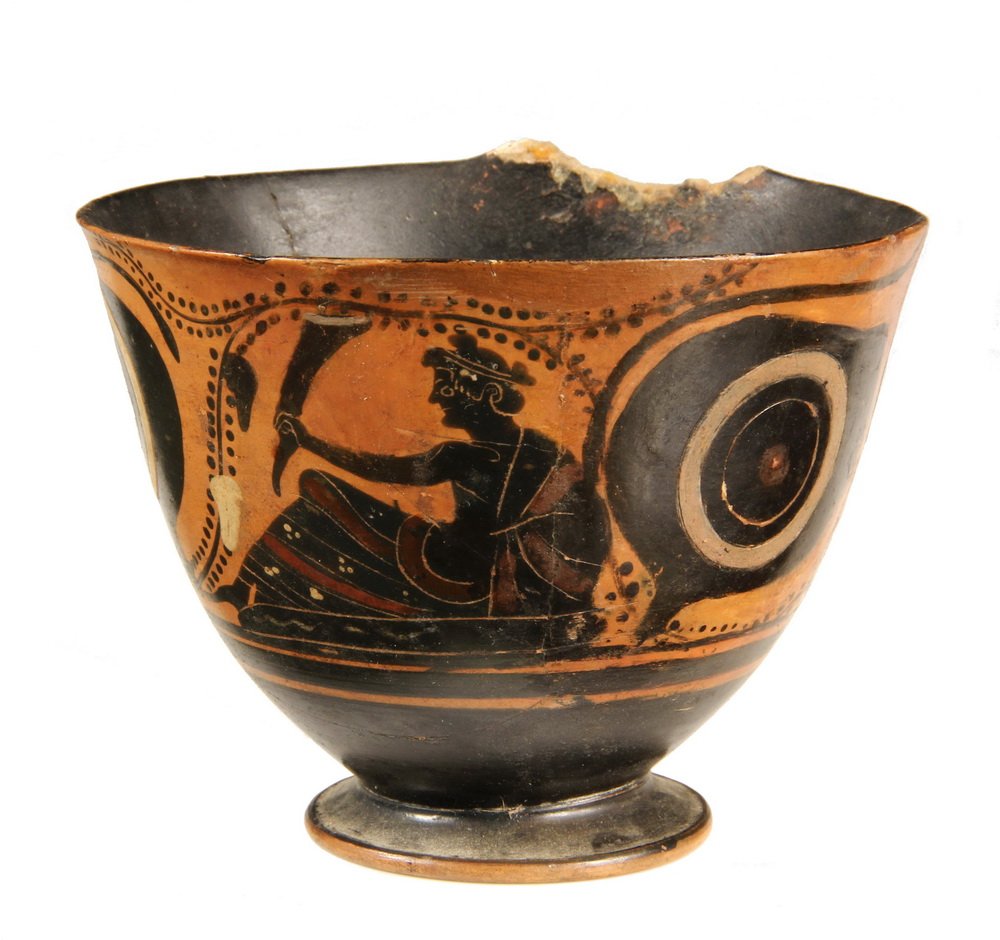 GREEK POTTERY CUP - Attic Black Figure Footed Cup,: GREEK POTTERY CUP - Attic Black Figure Footed Cup, circa 550 BC, depiciting a hero reclining on a couch, protected by shields from flanking Chimera, with black interior. 3 1/4" x 4 1/4" diam. Re-assem