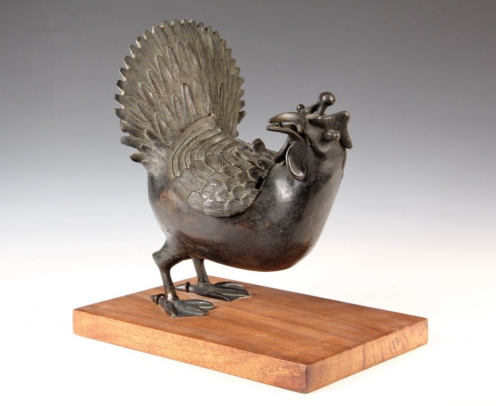 CHINESE BRONZE FIGURAL CENSER - Standing Figure of a: CHINESE BRONZE FIGURAL CENSER - Standing Figure of a Game Bird with head turned towards right, tail fanned out, the vented wings lift off for access to the interior. Mounted on wooden stand. 7" long.
