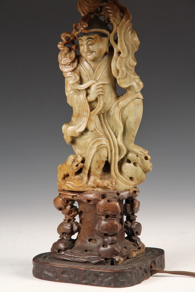 CHINESE SOAPSTONE FIGURE AS A LAMP - Circa 1920s: CHINESE SOAPSTONE FIGURE AS A LAMP - Circa 1920s Electric Table Lamp with Two-Piece Figure & Base of Traveler with Dog, mounted on wooden stand, with original silk shade. 12 3/4" tall figure, 24" tall