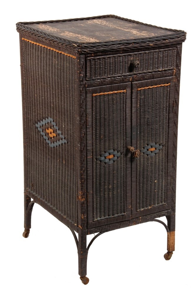 RARE WICKER VICTROLA STAND - Basketweave Cabinet with: RARE WICKER VICTROLA STAND - Basketweave Cabinet with drawer & two-door record storage, in black paint with orange & blue diamond decoration, on wooden casters. Circa 1910. 39 1/2" x 20" x 23". Loss t
