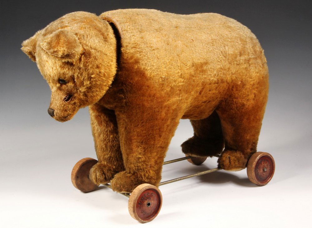 RIDING TOY - Schuco Yes/No Bear on wheels, circa 1930,: RIDING TOY - Schuco Yes/No Bear on wheels, circa 1930, in caramel mohair with glass eyes, wooden wheels stamped 'Schuco Patent', nodding head and wagging tail, pull-stem growler. 24" long, 16 1/2" tal
