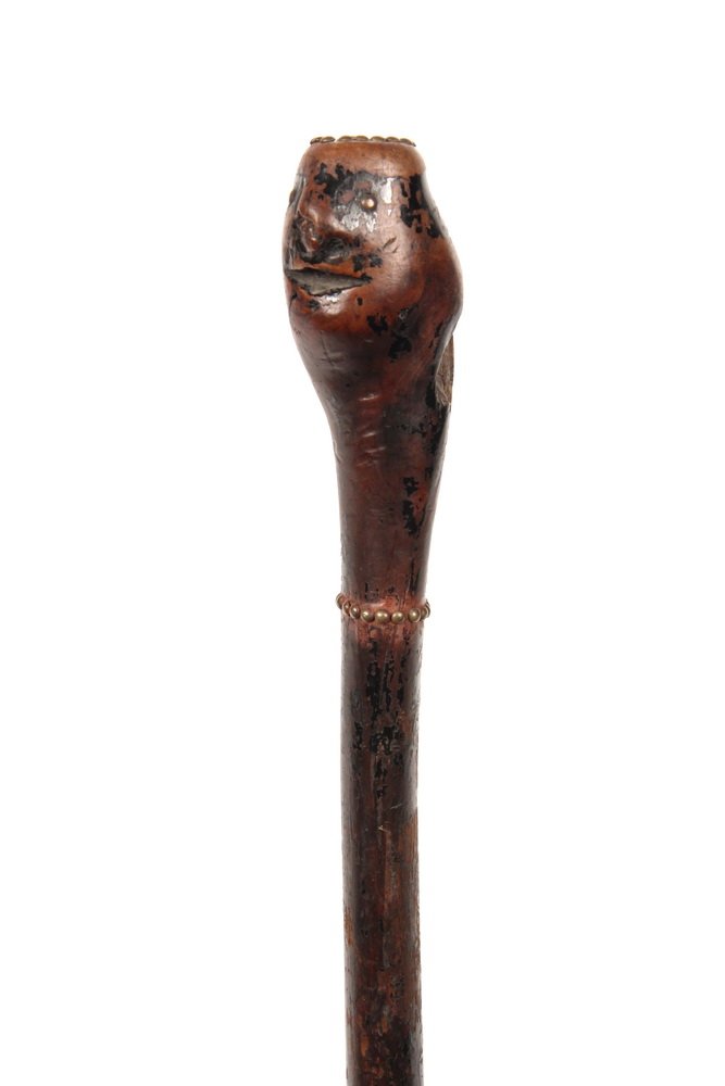 NATIVE AMERICAN WALKING STICK - 19th c Hickory Cane in: NATIVE AMERICAN WALKING STICK - 19th c Hickory Cane in remnants of black enamel paint, with handle in form of human head having open mouth, brass tack hair and collar, 31" long, worn, portion gone for