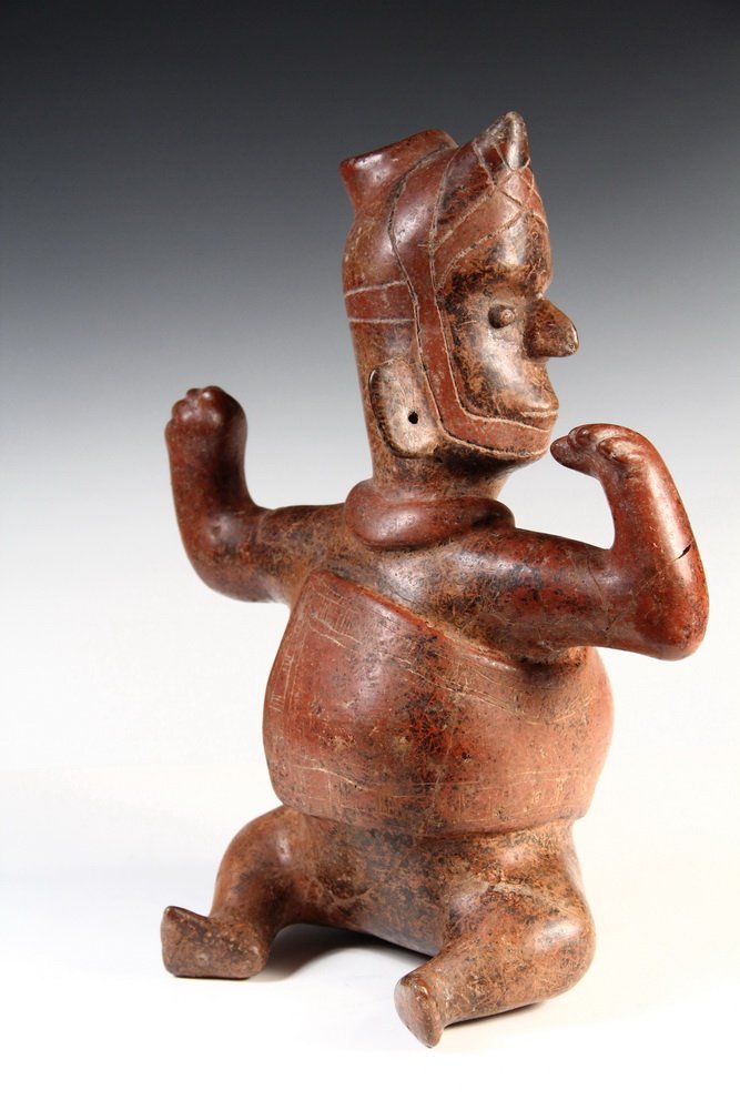 PRE-COLUMBIAN POTTERY - Mayan Terra Cotta Incise: PRE-COLUMBIAN POTTERY - Mayan Terra Cotta Incise Decorated Figural Decanter, a seated man in protective head gear (ball player?), wrapped in a blanket, seated with his arms partly raised, with pierced