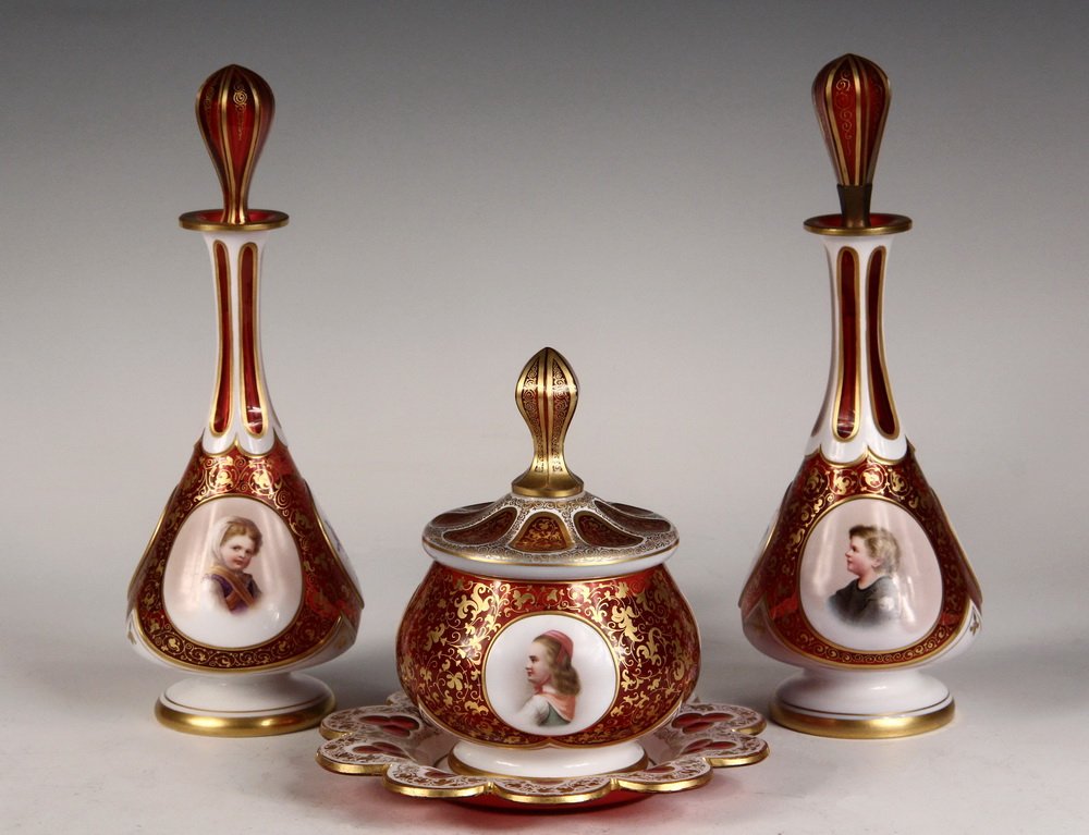 BAVARIAN CASED GLASS DRESSER SET - Powder Jar & (2): BAVARIAN CASED GLASS DRESSER SET - Powder Jar & (2) Decanters in White Cut to Cranberry Moser Style Glass, circa 1870-80, with gilt vinework and banding, white raised cartouches featuring boys and gir