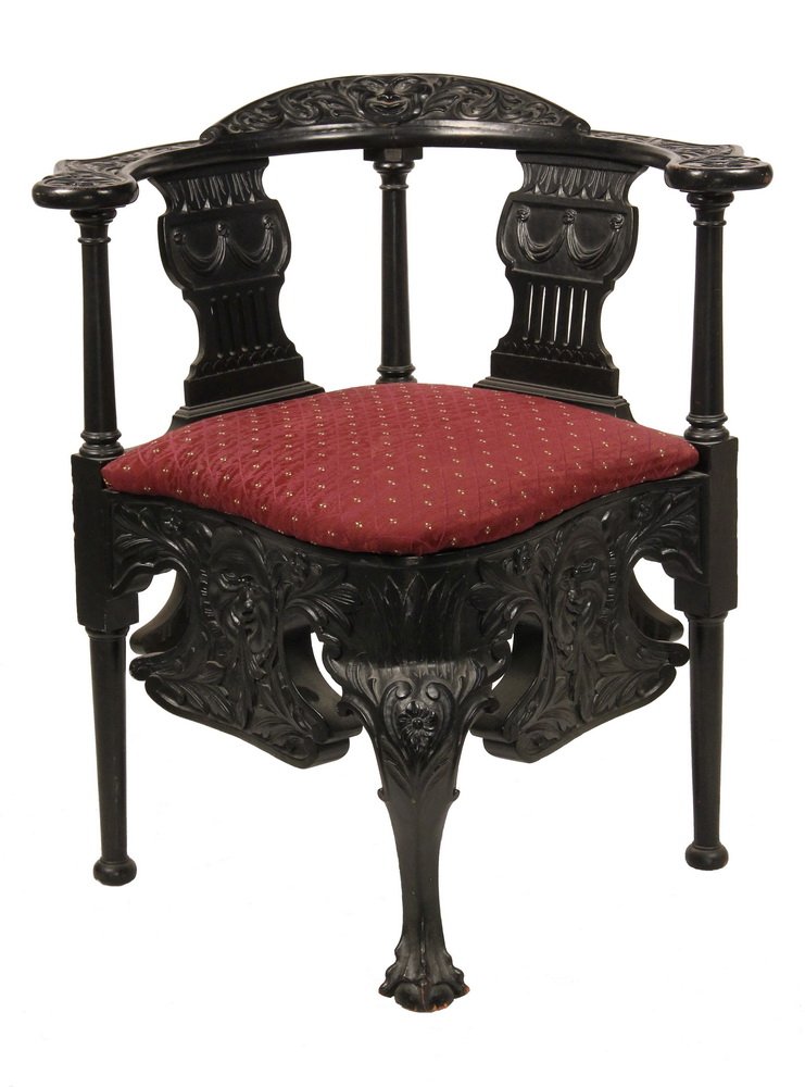 CORNER CHAIR - Ornately Carved Corner Chair, attributed: CORNER CHAIR - Ornately Carved Corner Chair, attributed to R.J. Horner, in black lacquered surface carved oak, with moon portraits on the rail pillow, arms and elongated skirts surrounded by acanthus