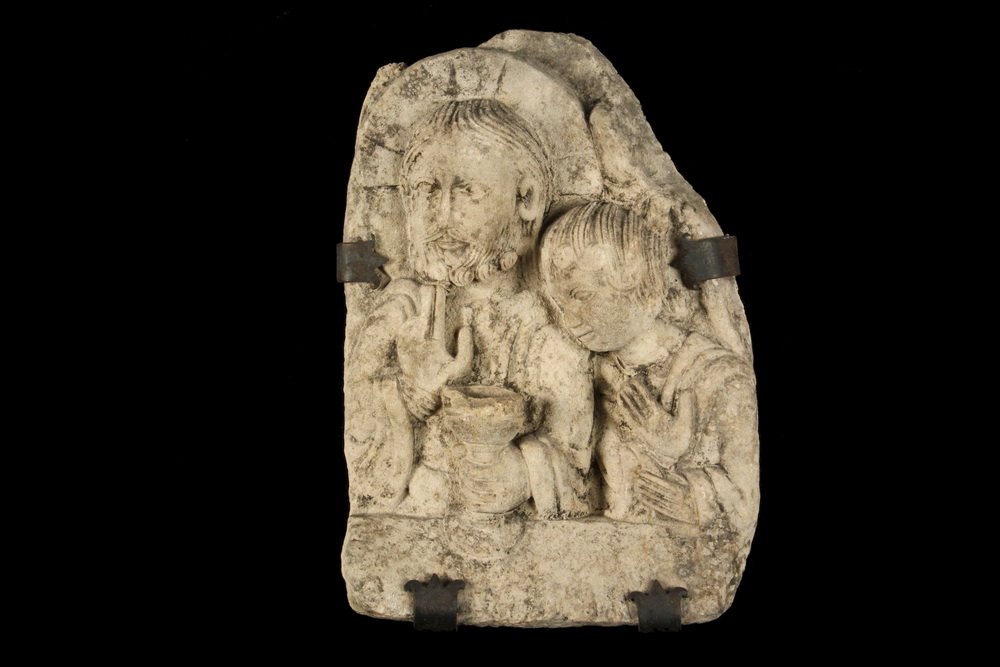 STONE BAS RELIEF - An Important French Romanesque: STONE BAS RELIEF - An Important French Romanesque Carved Stone Architectural Fragment, depicting Christ holding the Chalice of Life, one hand raised in benediction, with an Innocent Child at his shoul