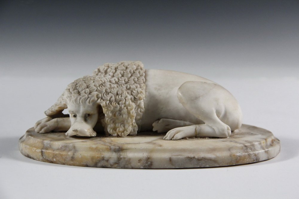 MARBLE DESKTOP CARVING - Late 18th to early 19th c.: MARBLE DESKTOP CARVING - Late 18th to early 19th c. French White Marble Carving of a Reclining Poodle Dog, mounted on a variegated oval molded plinth, the eyes and nose with touches of black. 6 1/2" l