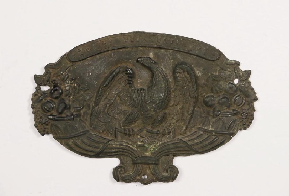 EARLY MILITARY SHAKO BRASS PLATE: Pressed Brass Militia Hat Placket, probably Connecticut, circa 1820, ovoid sheet brass plate embossed with a spreadwing eagle on a shield, flanked by cornucopia, with motto riband above "Ne Plus Ultra