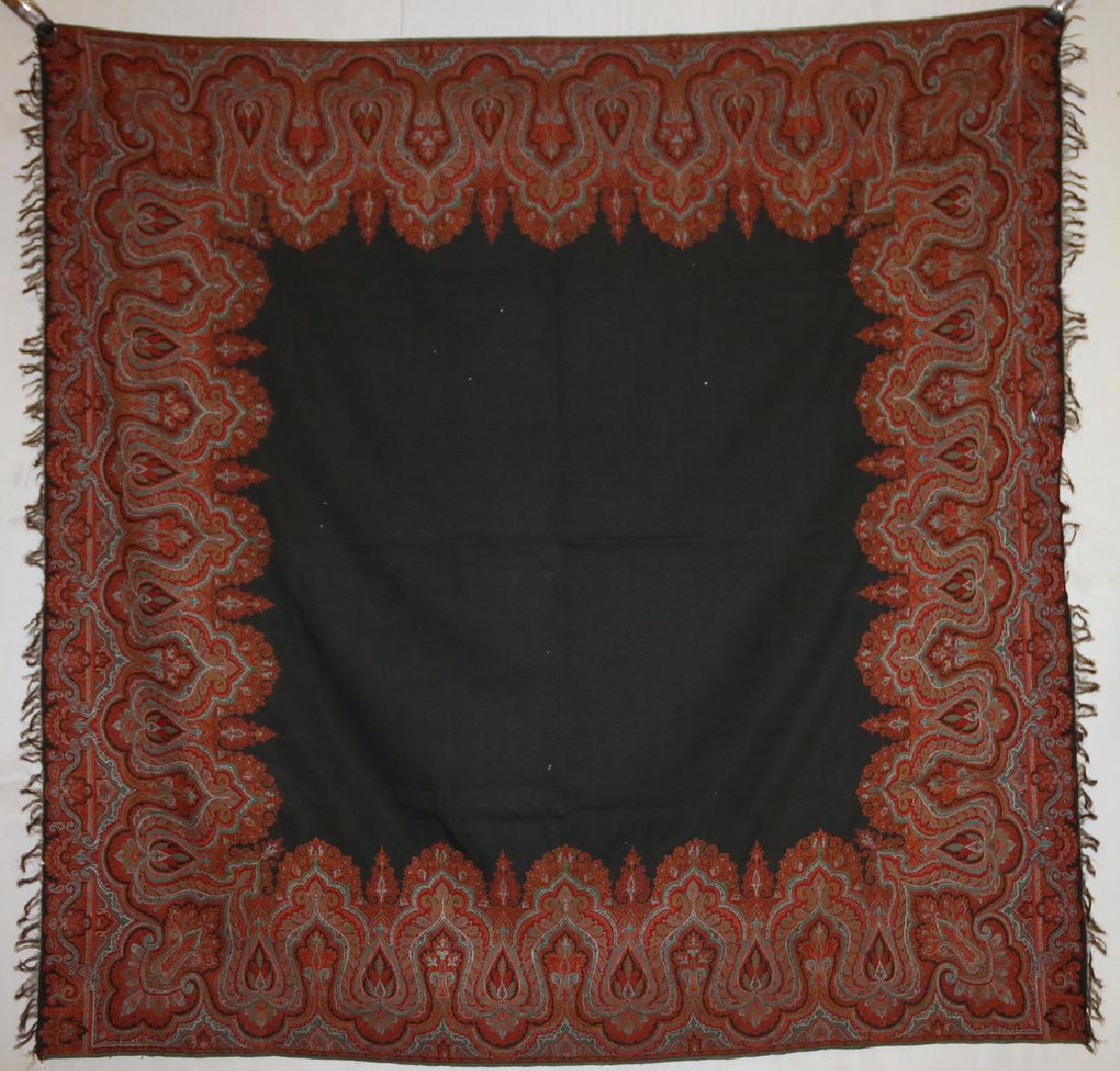 PAISLEY TEXTILE - 67" x 67": 19th c. Paisley Woven Wool Shawl or Tablecloth with black open central field, and decoration in reds, orange, green and white, black fringe on two sides. One 1/2" long tear in central field.