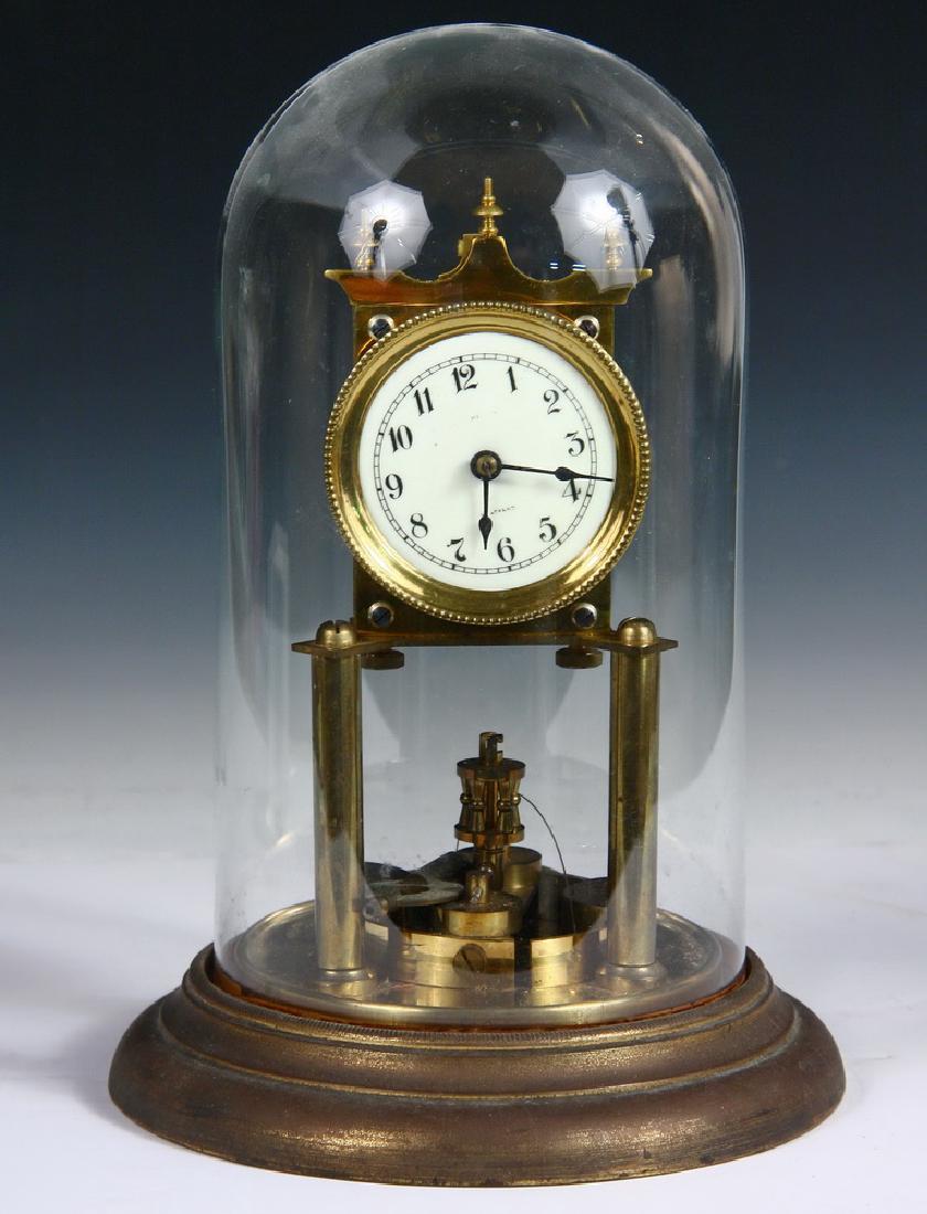 UNUSUAL ANNIVERSARY CLOCK: 400 Day Torsion Clock in brass, under a glass dome, having a flat disc pendulum, probably made by Gustav Becker of Germany, circa 1900, but the porcelain dial is only marked "34 Strand" (London salesr