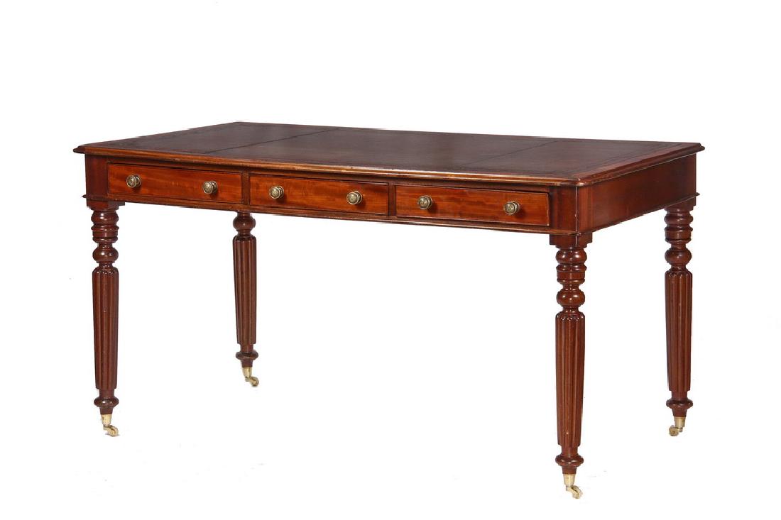 LEATHER TOP LIBRARY TABLE: Edwardian Table in figured mahogany with a tooled brown leather top, molded overhanging edge, molded case with three shallow beaded edge drawers having cast brass button pulls, ring and urn turned ree