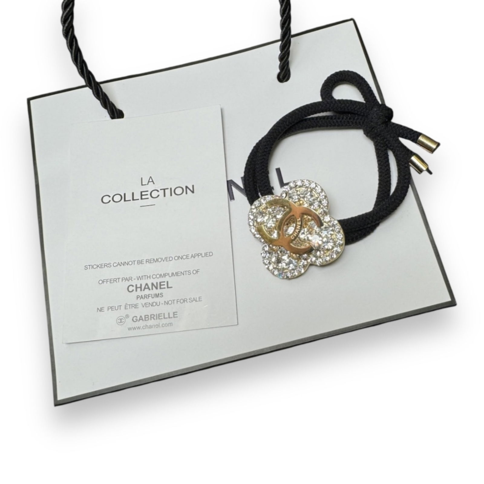 CHANEL White/Gold Rhinestone Accented Clover CC L.A Collection Hair Tie: • CHANEL• Gabrielle• White Rhinestones• Gold Accented Rhinestones• Clover Shaped• Black Tie• L.A Collection• Hair Tie • Gold Rhinestone CC Logo• Unope