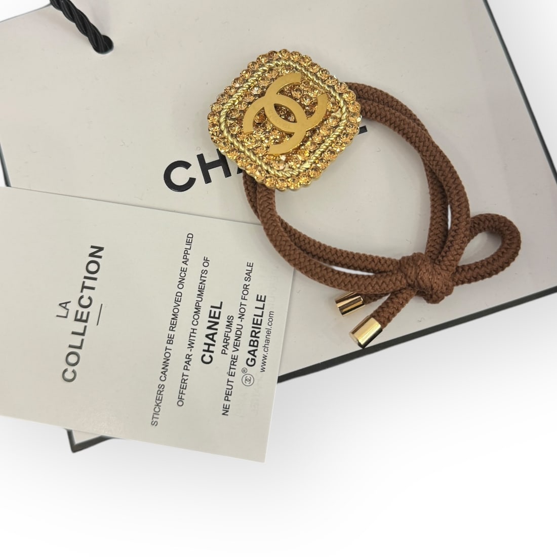 CHANEL Gold/Gold Rhinestone Accented Square CC L.A Collection Hair Tie: • CHANEL • Gabrielle • Gold Accented Rhinestones • Square Shaped • Brown Tie • L.A Collection • Hair Tie • Gold CC Logo • Unopened/In Original Packaging &b