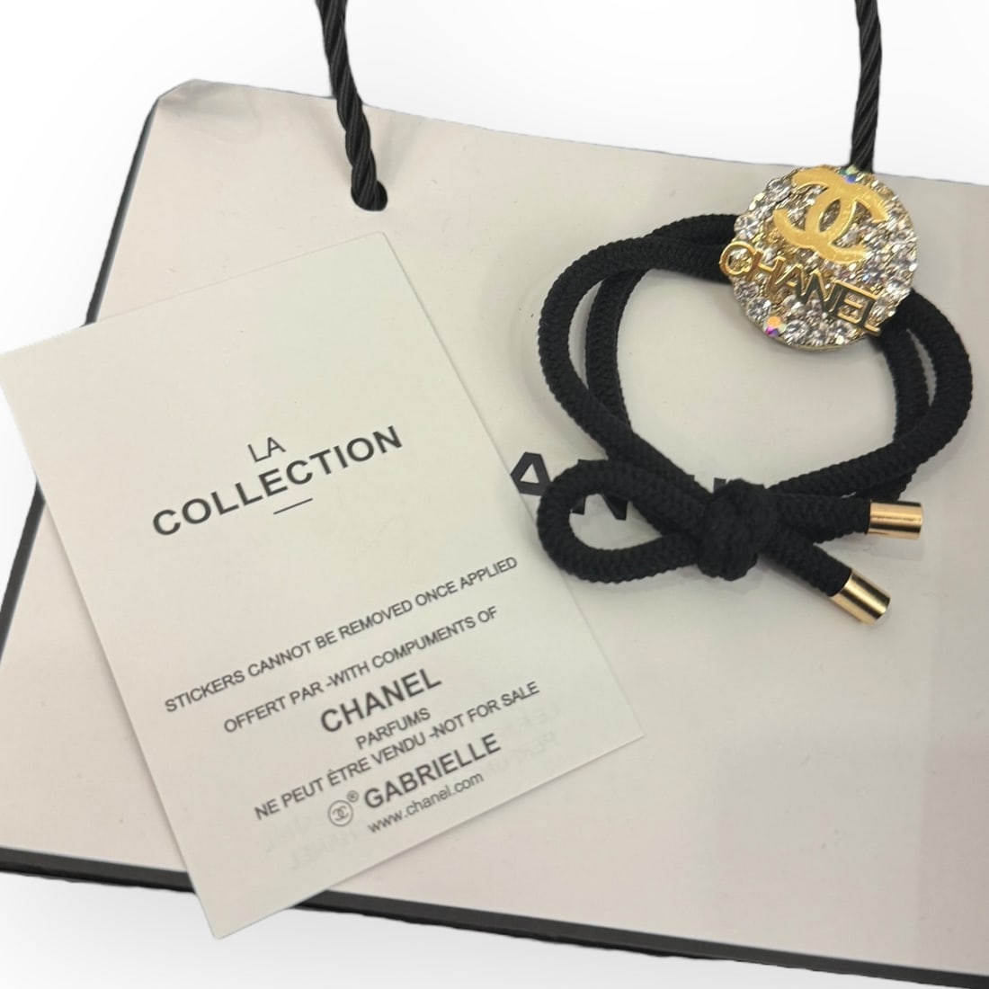 CHANEL White Rhinestone Round CHANEL/CC L.A Collection Hair Tie: • CHANEL • Gabrielle • White Rhinestones • Round Shaped • Black Tie • L.A Collection • Hair Tie • Gold CHANEL/CC Logo • Unopened/In Original Packaging &bul