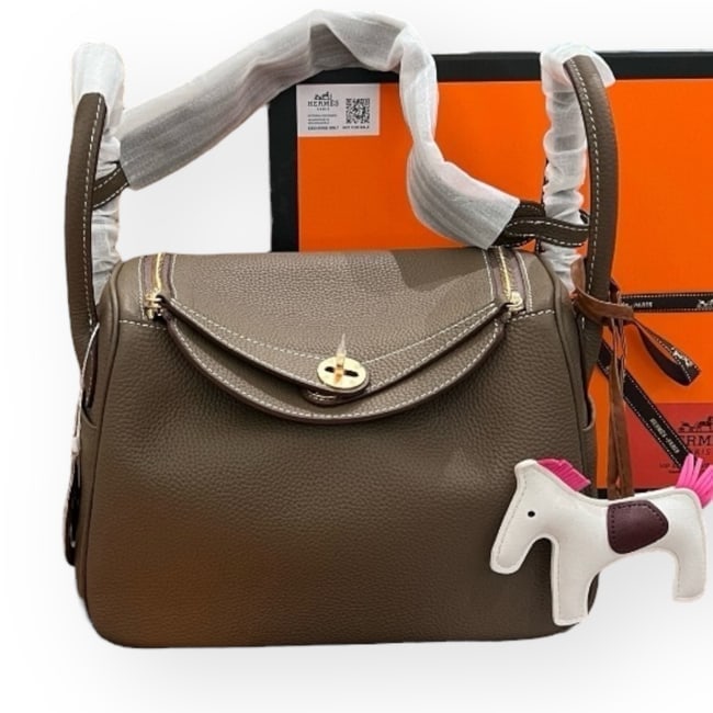 Hermes Lindy Bag Dark Tan Taurillon Pattern Beaute Bag & Original Box: • Hermes • Dark Tan • Taurillon Pattern • Lindy • Signature Front Twist Closure • Gold Tone Hardware • Zip Closure On Sides • Interior Slip Pocket • Side S