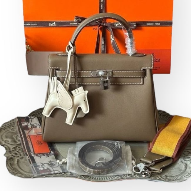 Hermes Kelly 25 Dark Tan/Silver 2Way Carry Beaute Bag, Strap, & Box: • Hermes • Kelly 25 • Dark Tan • Silver Tone Hardware • Signature Front Twist Lock Closure • Removable Strap Included • Top Handle Or Shoulder Carry • 10" x 7.5