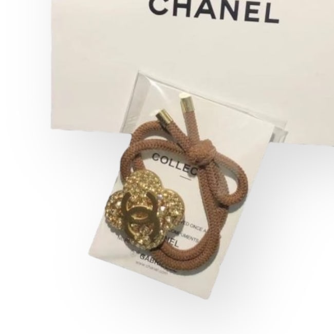 CHANEL Gold/Rhinestone Covered Clover CC Hair Tie & Gift Bag: • CHANEL • Gabrielle • Hair Tie • Gold Tone Hardware • Gold Rhinestones • Shape: Clover • Tie Color: Brown • L.A Collection • CC Logo • Unopened/I