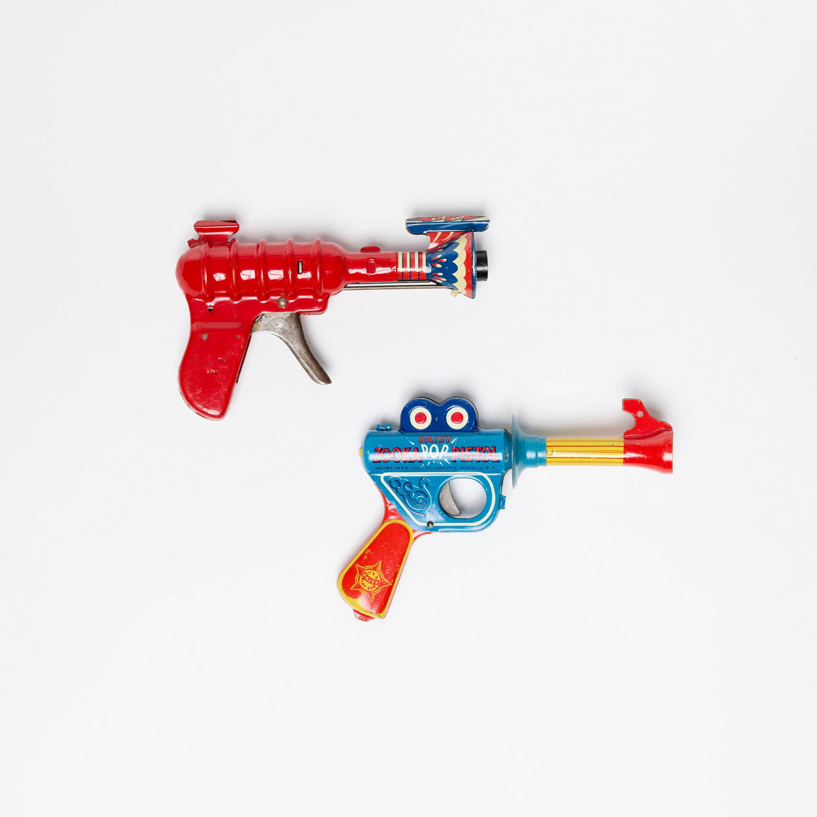 Two American Pressed Steel Ray Guns: Two American Pressed Steel Ray Guns transfer printon metal, zinc-plated steel 5.25 h x 7.5 w x 1.625 d in (13 x 19 x 4 cm) 4.5 h x 7 w x 1.5 d in (11 x 18 x 4 cm) Includes a Wyandotte 33 Repeater and